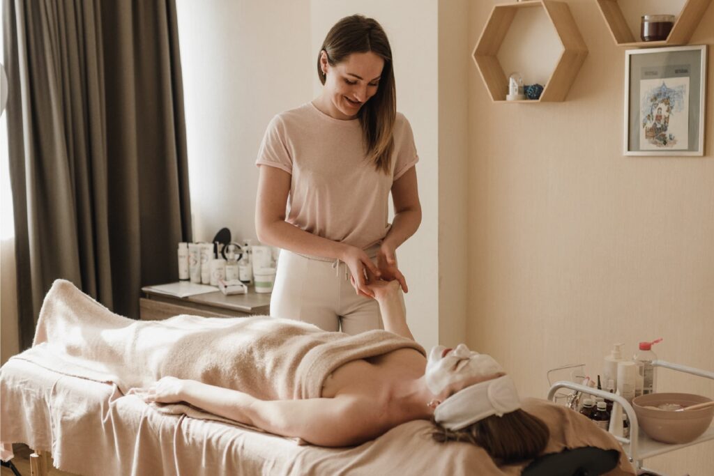 The client lies on a massage table, while the masseuse's skilled hands work on her hand.